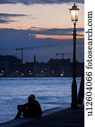 View of Canale della Giudecca, with young couple silhouetted, sitting beside illuminated wrought iron lamp on quayside, looking towards Giudecca, twilight, autumn in Venice, Northern Italy