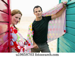Couple with towels relax by beach huts Couple with towels relax by beach huts