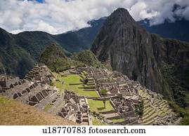 Machu Picchu Inca ruins : view of Eastern Urban sector and Royal Palaces and Temple of the Sun, with Huayna Picchu beyond, as seen from Sun Gate trail afternoon sunlight after storm, Machu Picchu, Sacred Valley, Peru