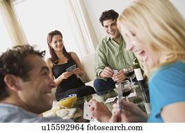 Couples on sofa at home party playing cards