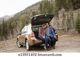 Portrait of young couple sitting in car trunk in non-urban scene