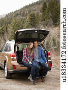 Portrait of young couple sitting in car trunk in non-urban scene