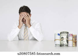 Worried businessman at table with money rolls representing financial problems