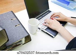 Close up of womans hands typing on laptop with folders and mug
