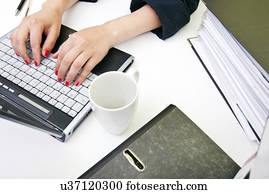 Close up of womans hands typing on laptop with folders and mug