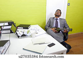 Indian businessman asleep at his desk clutching ukulele