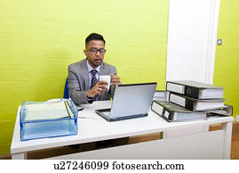 Portrait of Indian Businessman holding mug and working on his laptop computer at his desk
