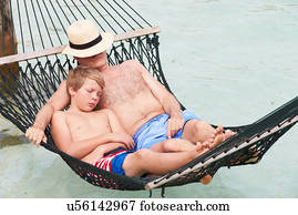 Grandfather And Grandson Relaxing In Beach Hammock 
