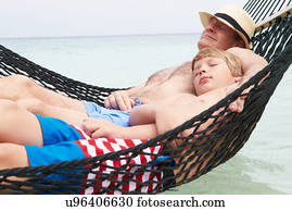 Grandfather And Grandson Relaxing In Beach Hammock 