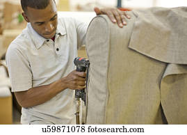 Upholsterer attaching textile to sofa using staple gun