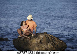 Father and daughter, sitting on rock in sea, Costa Brava, Catalonia, Spain