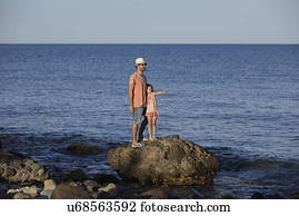 Father and daughter standing on rock in sea, Costa Brava, Catalonia, Spain