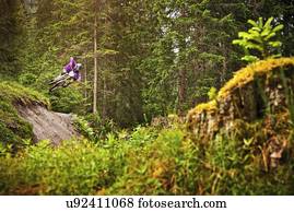Young male mountain biker jumping over forest gully