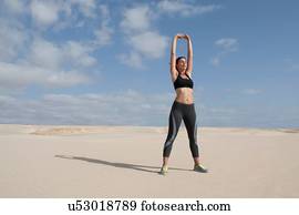 Mid adult woman exercising with arms raised on beach