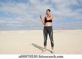Mid adult woman selecting headphone music whilst exercising  at beach