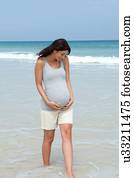 Pregnant mid adult woman paddling in sea with hands on stomach