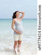 Pregnant mid adult woman standing in sea with eyes closed and hand on stomach