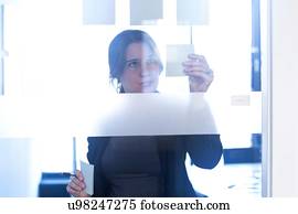 Businesswoman sticking notes on glass wall in office