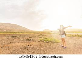 Young woman with arms open in sunlit volcanic landscape, La Oliva, Fuerteventura, Spain