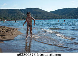 Boy paddling in lapping waves on coastline, Italy