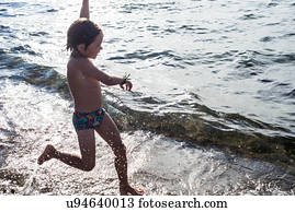 Boy paddling in lapping waves on coastline
