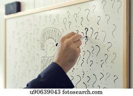 Businessman writing question marks on office whiteboard.