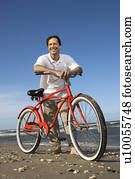 Caucasian mid-adult man posing with red bicycle on beach.