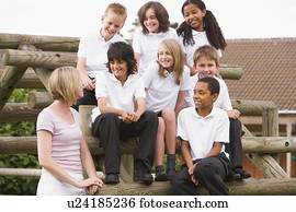 Seven students sitting on wooden structure with teacher standing beside them