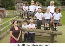 Students sitting outdoors on wooden structure with teacher standing beside them