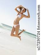 Woman in a two piece bathing suit jumping on a beach