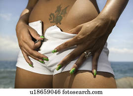 Multi ethnic young adult woman on beach unzipping shorts.