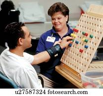 Man with a disability putting pegs in a board during a session with his occupational therapist. Man with a disability putting pegs in a board during a session with his occupational therapist.