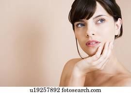 Portrait of a young woman with dark hair in a bun, chin in her hand, thinking