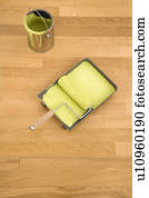 Still life of paint roller in tray with paint can on wood floor.