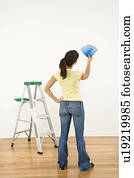 Woman standing in front of white interior wall with paint sample cards trying to choose color.