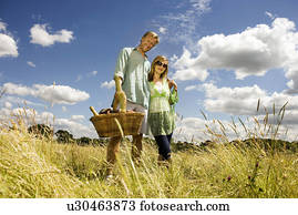 https://cdn-grid.fotosearch.com/UNW/UNW874/couple-with-picnic-basket-in-field-stock-photo__u30463873.jpg