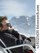 Man in winter coat and sunglasses sitting in arm chair by mountains
