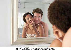 Man embracing woman applying lipstick in mirror