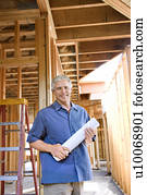 Caucasian mid-adult male holding blueprints in building construction site.