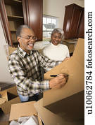 Middle-aged African-American male labeling moving box with wife in background.
