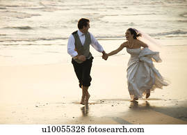 Caucasian prime adult male groom and female bride running barefoot on beach.