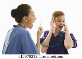 Portrait of Caucasian healthcare workers wearing scrubs with one yelling into stethoscope that is attached to other's ears against white background. Portrait of Caucasian healthcare workers wearing scrubs with one yelling into stethoscope that is attached to other's ears against white background.