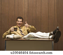 Caucasion mid-adult retro businessman sitting with feet propped on desk drinking coffee giving a thumbs up.
