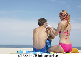 Woman applying sunscreen on man's back at beach