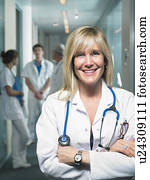 Group of four doctors in a lobby of a hospital. Female doctor in foreground. Smiling. Group of four doctors in a lobby of a hospital. Female doctor in foreground. Smiling.