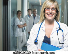 Group of four doctors in a lobby of a hospital. Female doctor in foreground. Smiling. Group of four doctors in a lobby of a hospital. Female doctor in foreground. Smiling.