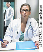 Portrait of female doctor at her desk with male doctor in background. Portrait of female doctor at her desk with male doctor in background.