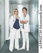 Two female doctors looking at camera in a lobby of a hospital smiling. Two female doctors looking at camera in a lobby of a hospital smiling.