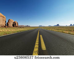 Open highway in scenic desert landscape with distant mountains and butte land formations.