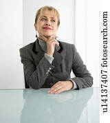 Woman sitting at desk with hand to chin smiling and making facial expression